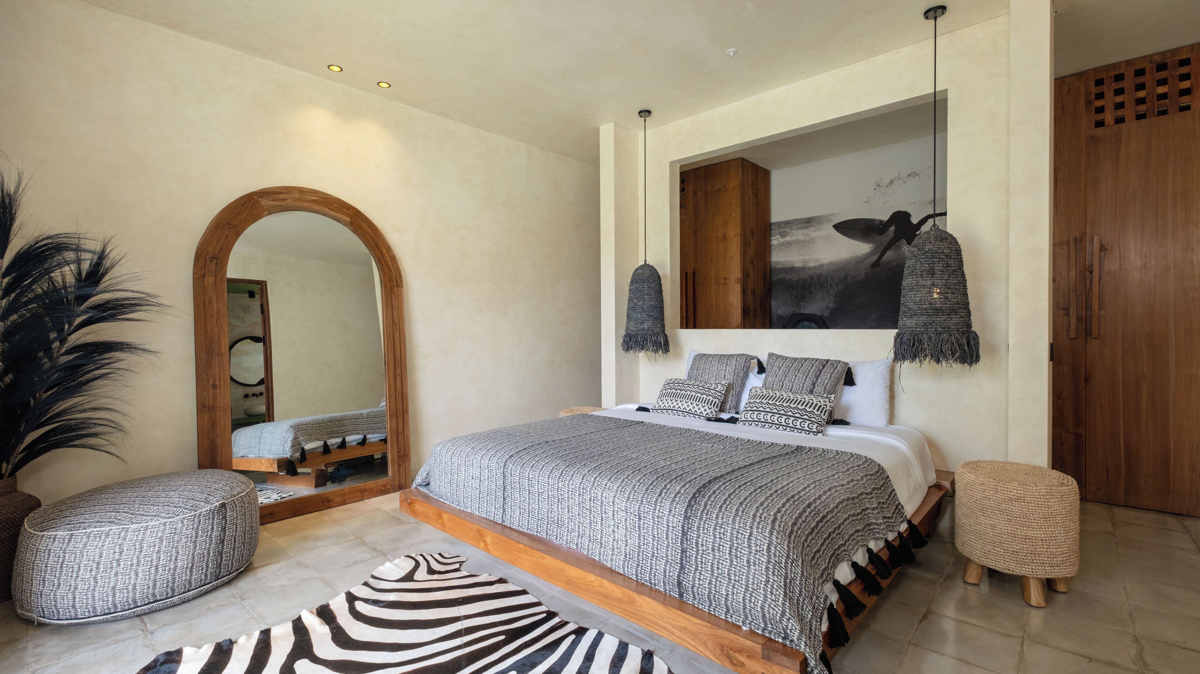 A bedroom with a large bed, a wooden wardrobe, a mirror, and a hanging light fixture.