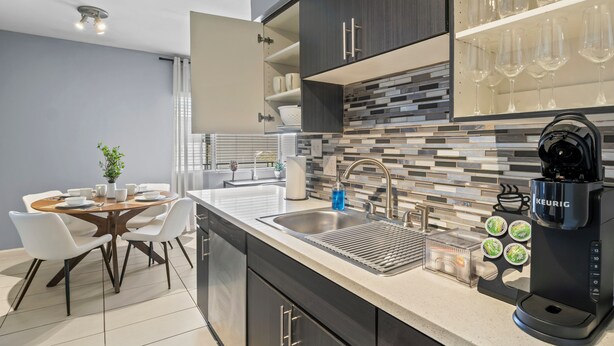 Una cocina moderna con cafetera integrada, un lavamanos y una zona de comedor con mesa y sillas.