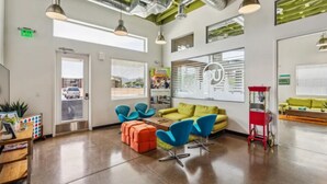 Un área de recepción moderna con un sofá verde, sillas azules y un carrito rojo.
