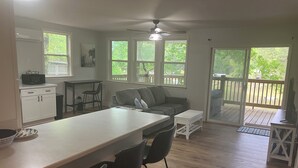 Eine geräumige Küche mit Kochinsel, ein Essbereich mit einer Couch und Blick auf eine Holzterrasse.