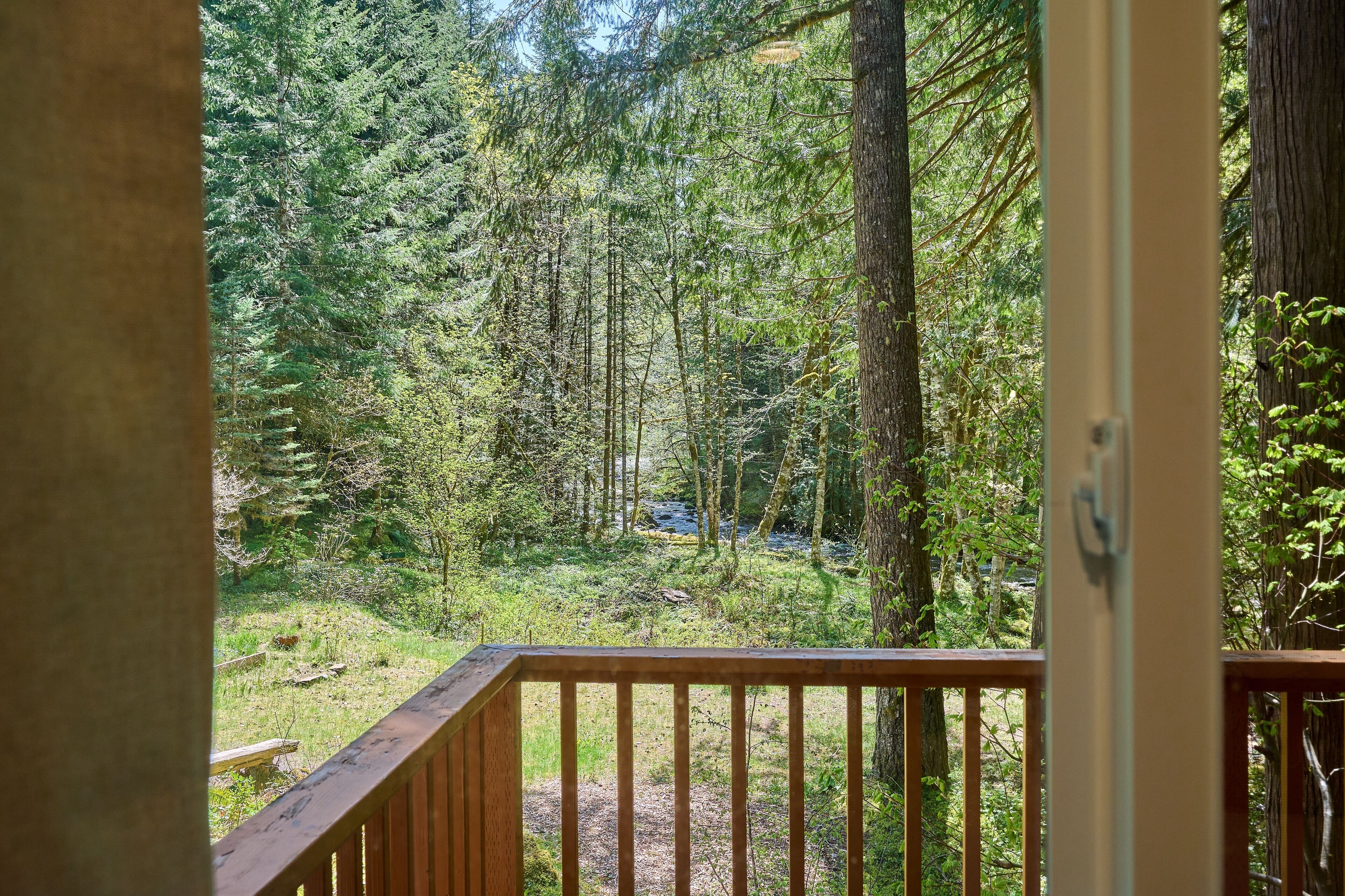 A wooden deck with a view of a dense forest and a stream.