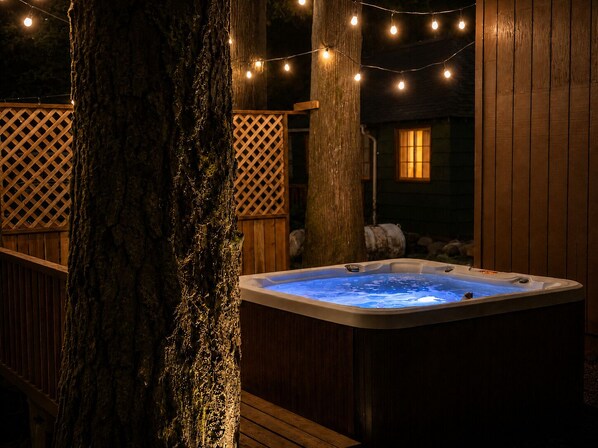 A hot tub surrounded by wooden deck and lattice panels, with string lights overhead.