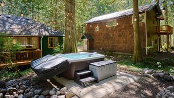 A cabin with a hot tub, surrounded by trees and a wooden deck.