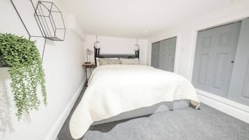 A bedroom with a bed, a grey carpet, a grey door, and a green plant on the wall.