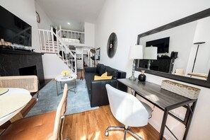Een moderne woonkamer met een bank, een eettafel en een televisie. Er is een trap die naar een hoger gelegen verdieping leidt.