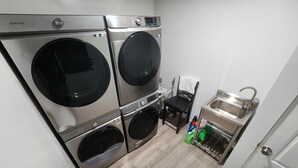 A compact laundry area with two stacked washing machines, a chair, and a sink. - Tinyhouse with AC and laundry area. Near Ector County Coliseum (Odessa)