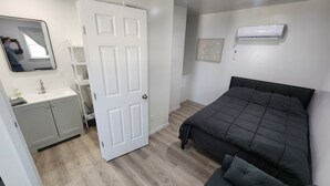 A bedroom with a bed, a bedside table, a wardrobe, a mirror, and an air conditioning unit. - Tinyhouse with AC and laundry area. Near Ector County Coliseum (Odessa)