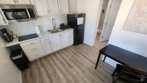 A compact kitchen with white cabinets, a black refrigerator, a microwave, and a sink. There's a wooden floor and a small dining table with chairs. - Tinyhouse with AC and laundry area. Near Ector County Coliseum (Odessa)