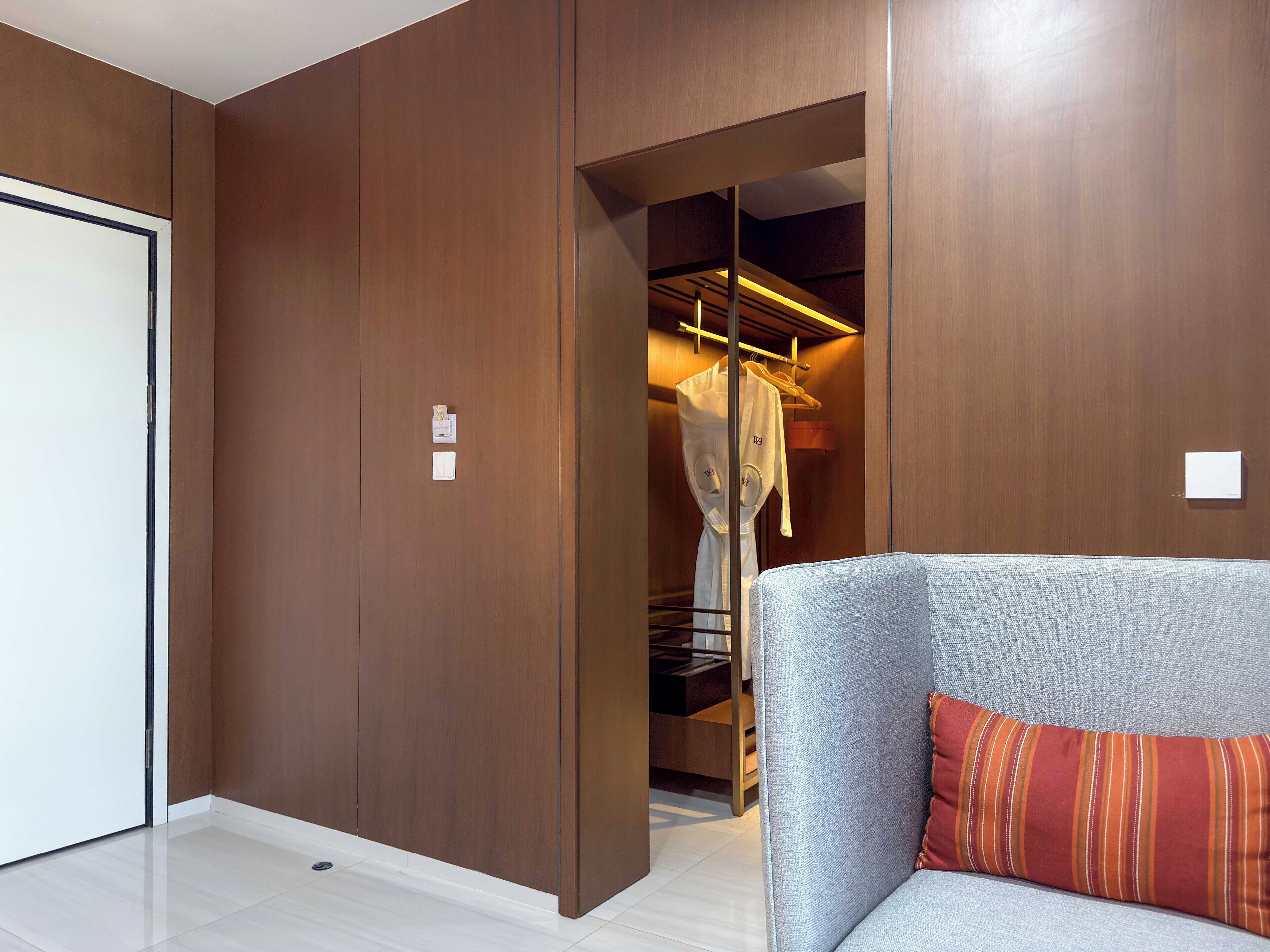 Une chambre d’hôtel moderne avec un canapé gris, un coussin à rayures et une armoire en bois.