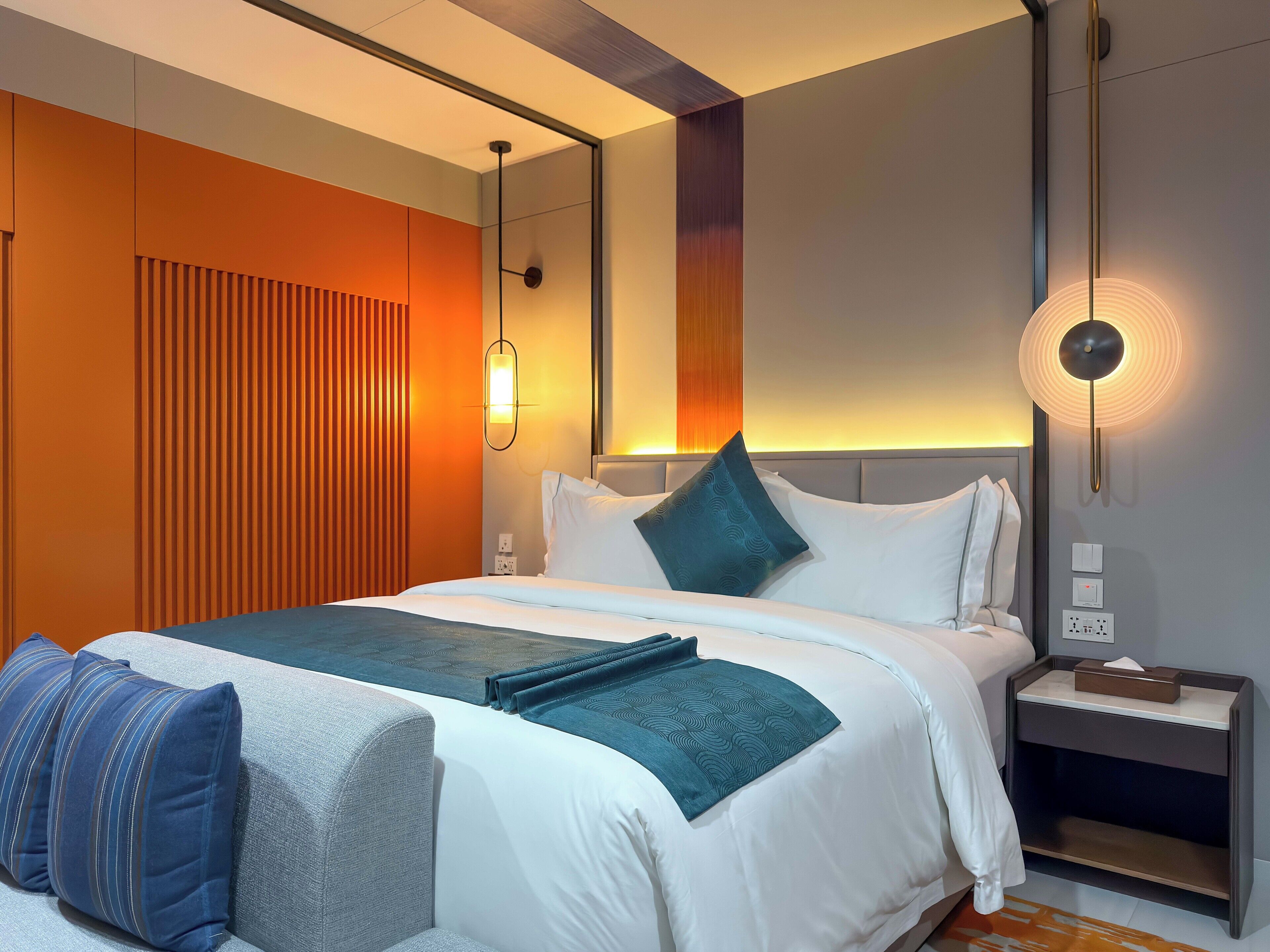 Une chambre d’hôtel moderne avec un grand lit, une table de chevet et un luminaire fixé au mur.