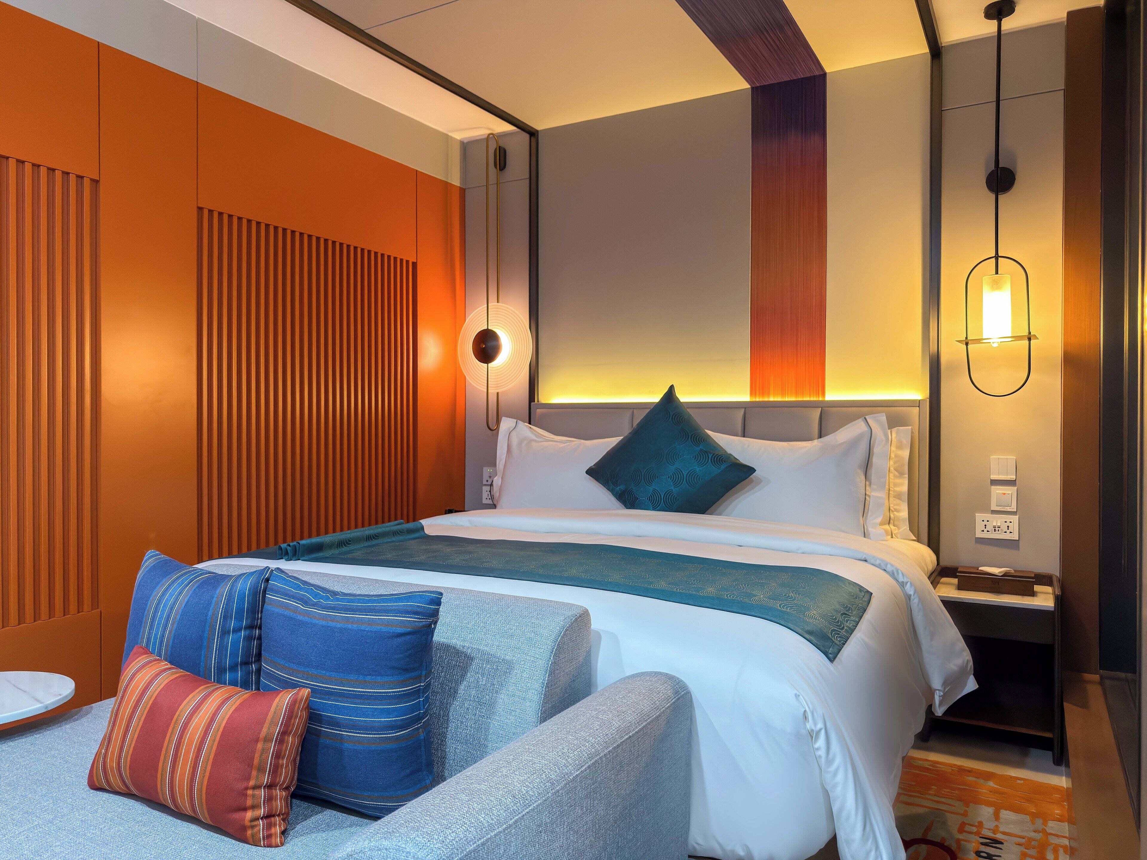 Une chambre d’hôtel moderne dotée d’un grand lit, d’un coin salon avec un fauteuil et une petite table, ainsi que d’une table de chevet avec une lampe.