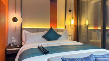 A modern hotel room with a neatly made bed, a bedside table with a phone, and a wall-mounted lamp.
