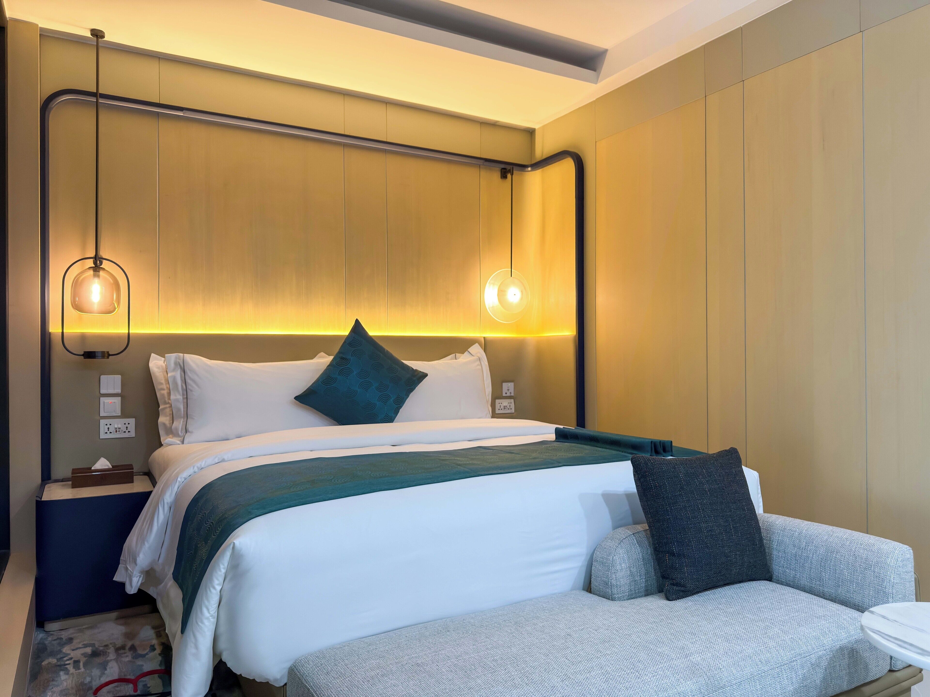 Una habitación de hotel moderna con una cama bien hecha, un sofá y dos lámparas colgantes.