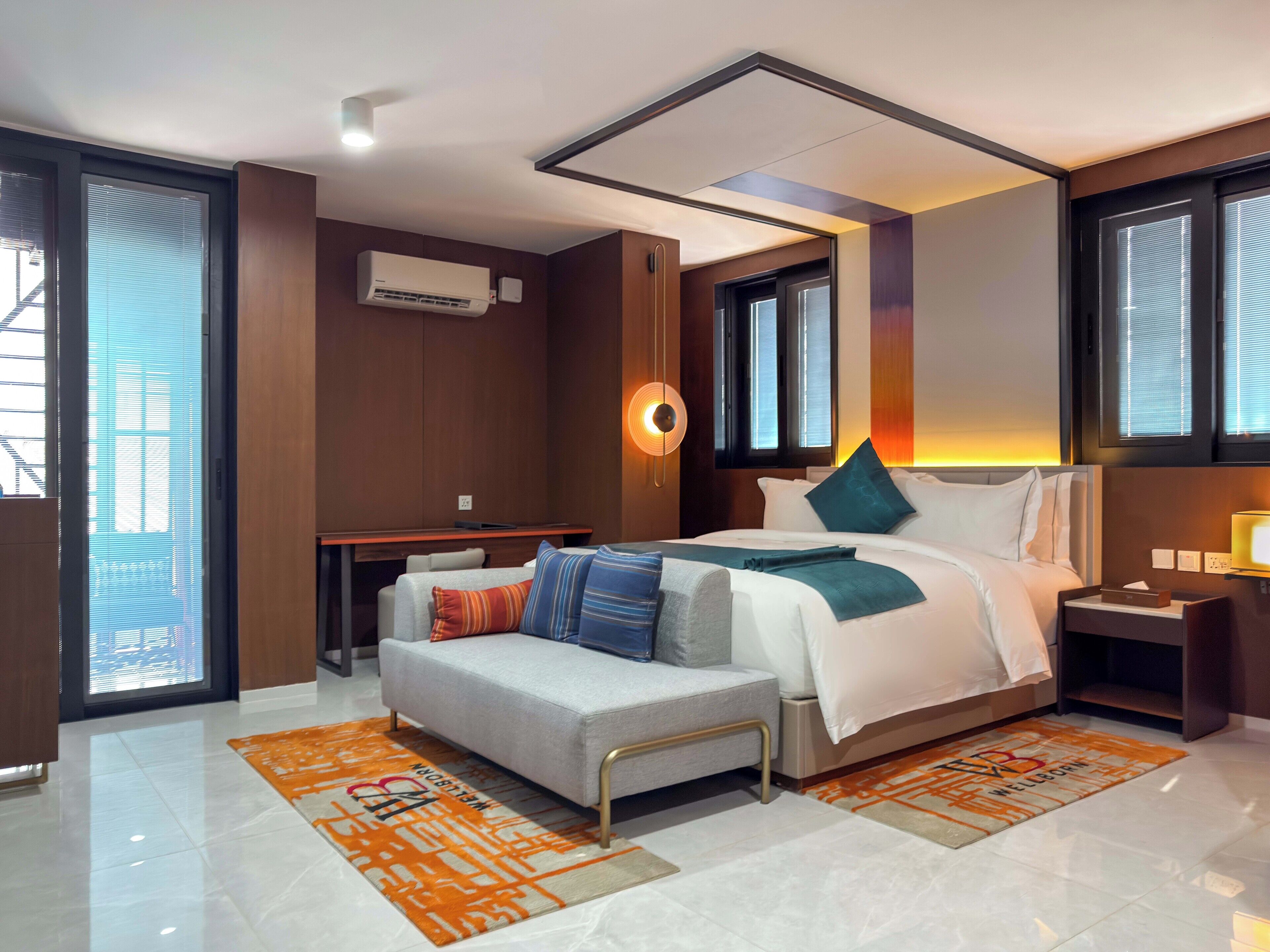 A modern hotel room with a large bed, a sofa, a desk, and a window with blinds.