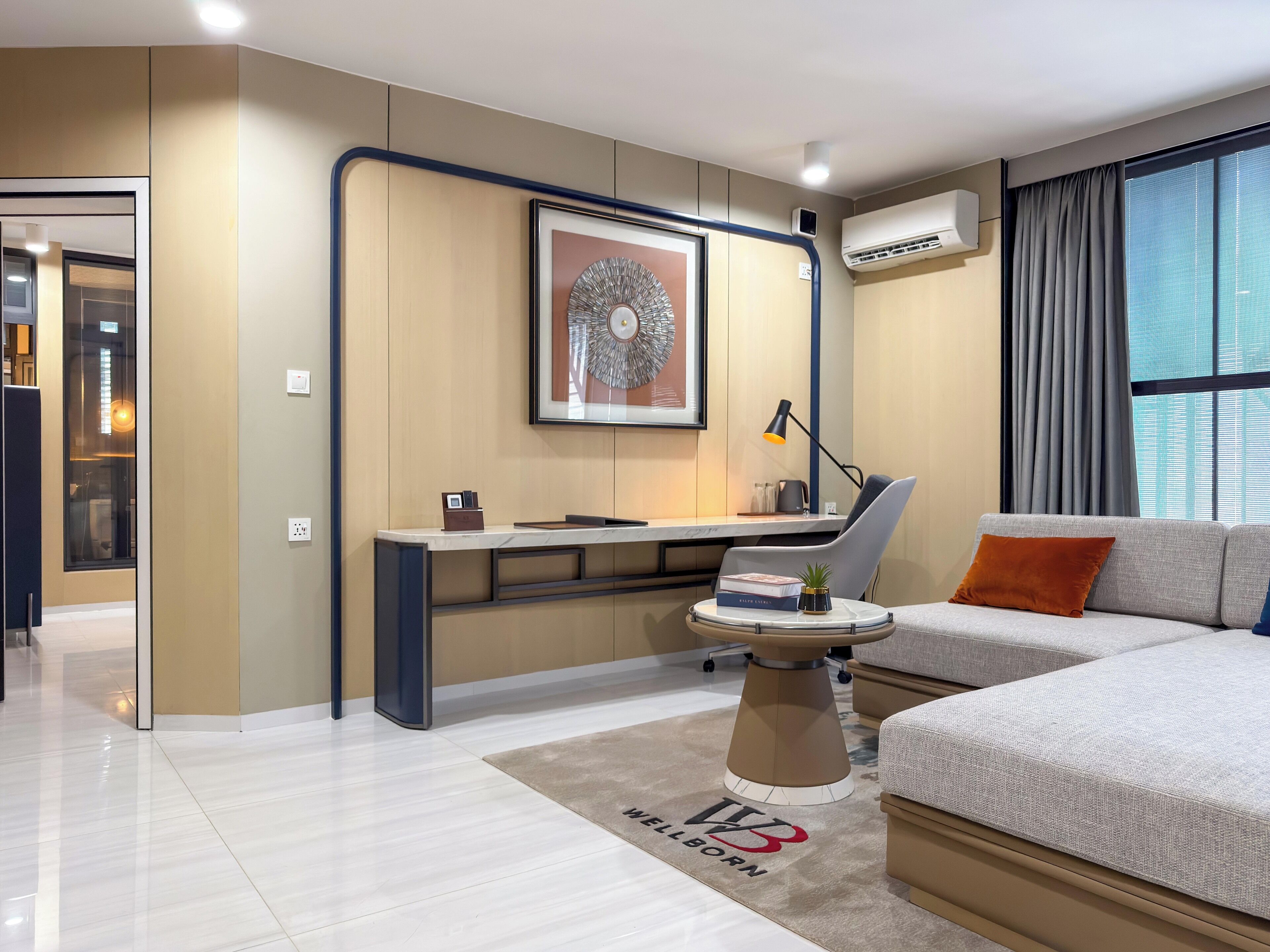 Ein modernes Schlafzimmer mit Bett, Schreibtisch und Stuhl. Ein Fenster mit Vorhängen, eine Wand-Klimaanlage und ein gerahmtes Kunstwerk über dem Schreibtisch.