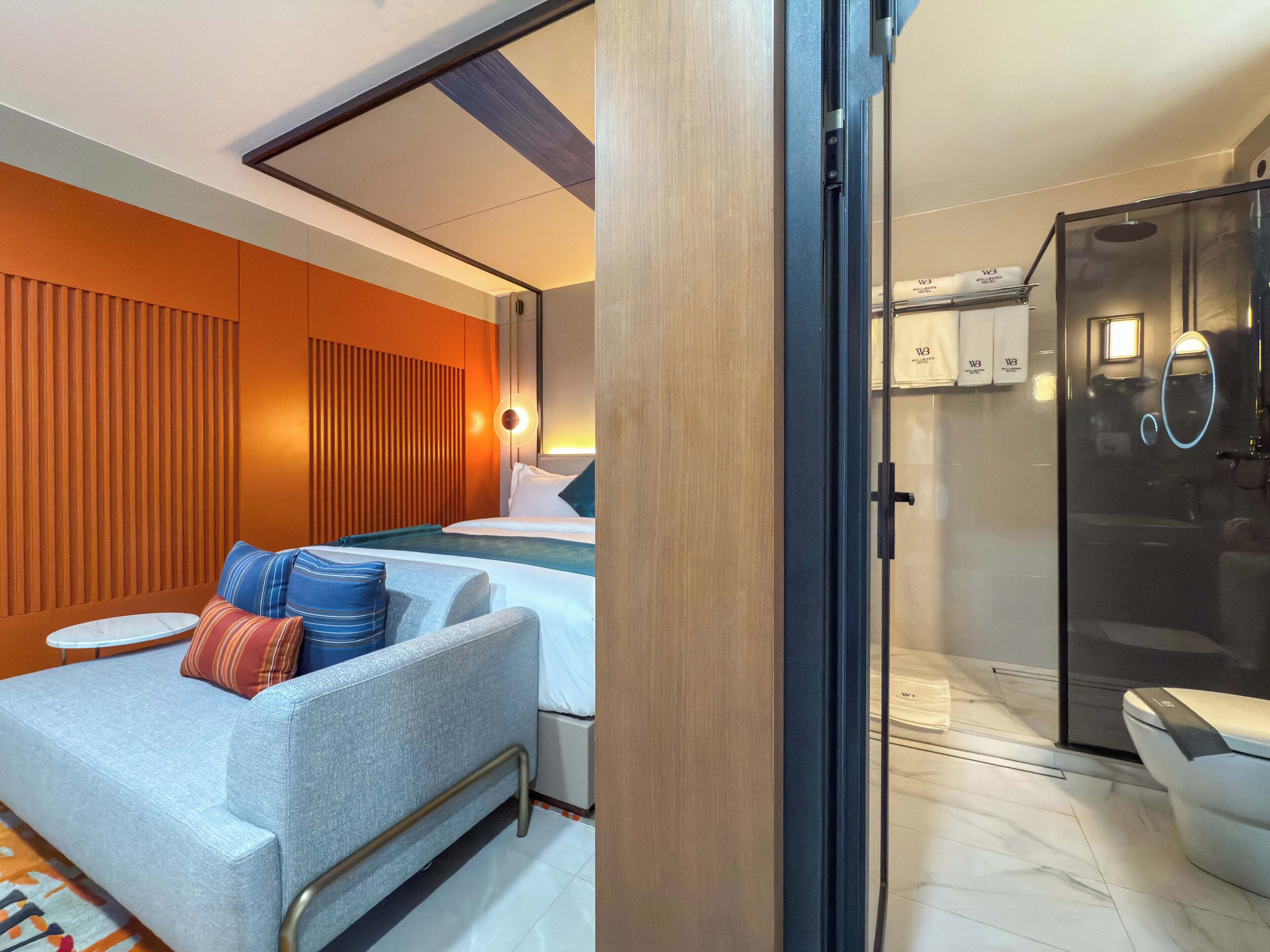 A modern hotel room with a sofa, a bed, a small table, and a bathroom with a toilet and shower.