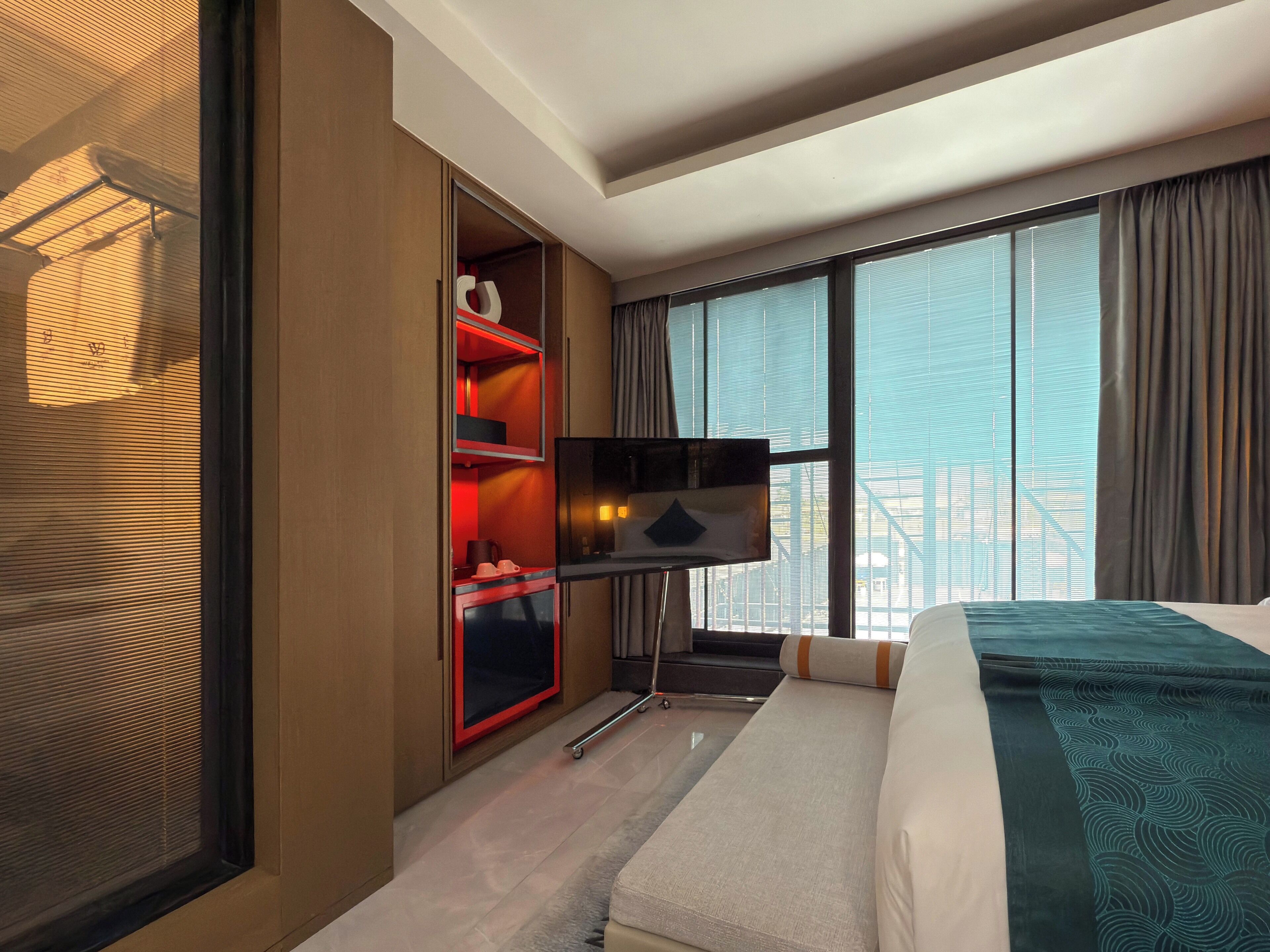 Une chambre d’hôtel avec un lit, une télévision, une armoire et une grande fenêtre avec des rideaux.