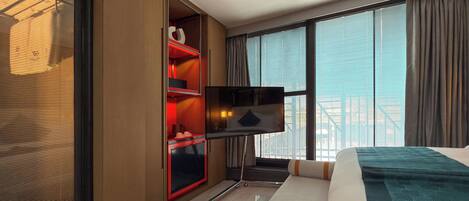 Une chambre d’hôtel avec un lit, une télévision, une armoire et une grande fenêtre avec des rideaux.