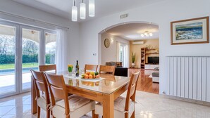 Un vaste espace dédié à la salle à manger, avec une table et des chaises en bois, un panier de fruits et une vue sur l’extérieur.