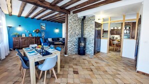 A dining area with a wooden table and chairs, a stone wall, and a kitchen visible through an open doorway. - Proche Océan, forêt et commerces by Interhome (Fromentine)