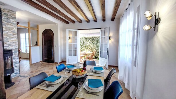 A dining area with a wooden table set for four, surrounded by chairs. There is a large window with a view of greenery outside. - Proche Océan, forêt et commerces by Interhome (Fromentine)