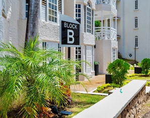 A building with a sign reading 'BLOCK B' and a well-maintained garden with palm trees.