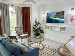 A living room with a sofa, a chair, a coffee table, a TV, and a plant. - Falcon CoralReef-Gated-24/7 Security-Airport Transport (Montego Bay)