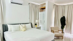 A bedroom with a large bed, a bedside table with a lamp, a chair, and a potted plant. - Falcon CoralReef-Gated-24/7 Security-Airport Transport (Montego Bay)
