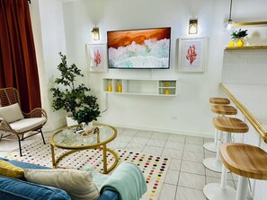 A modern living room with a TV, wicker chair, round coffee table, potted plants, and a colorful rug. - Falcon CoralReef-Gated-24/7 Security-Airport Transport (Montego Bay)