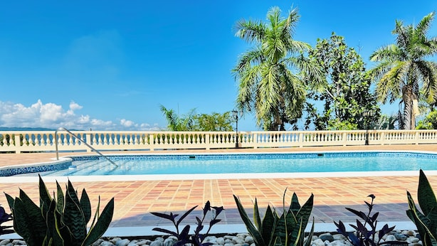 A swimming pool with a tiled deck, surrounded by palm trees and a white balustrade. - Falcon CoralReef-Gated-24/7 Security-Airport Transport (Montego Bay)