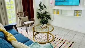 A living room with a sofa, a chair, a TV, a plant, and a round coffee table. - Falcon CoralReef-Gated-24/7 Security-Airport Transport (Montego Bay)