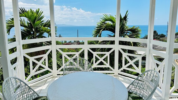 A covered outdoor area with a round table and two chairs, overlooking a coastal view.