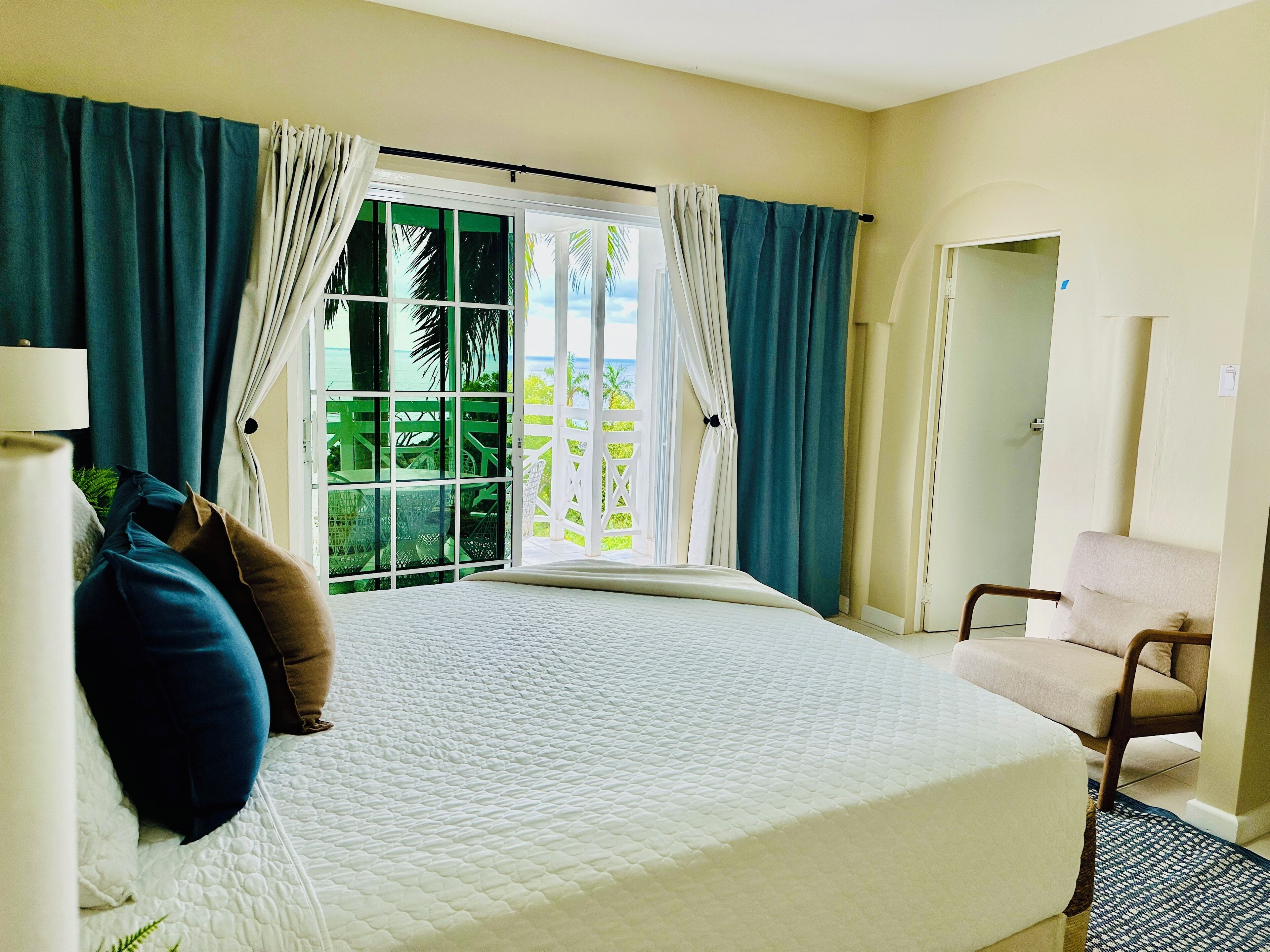 Habitación de hotel con cama, una silla, una lámpara y vistas a zonas verdes por una ventana.