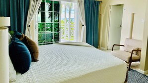 A hotel room with a bed, a chair, a lamp, and a view of greenery through a window.