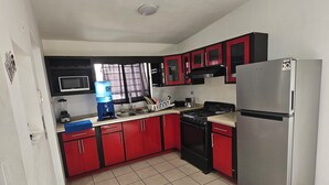 A compact kitchen with red cabinets, a stainless steel refrigerator, a microwave, and a stove. - Full house in subdivision (Juárez)