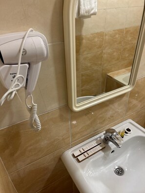 Une salle de bain avec un lavabo blanc, un miroir et un sèche-cheveux fixé au mur.