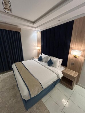 Une chambre d’hôtel moderne avec un grand lit, des rideaux foncés et deux lampes de chevet.