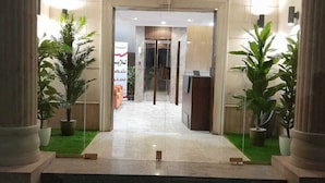 L’entrée d’un hôtel, avec un comptoir de réception, des plantes en pot et une porte vitrée donnant sur l’intérieur.