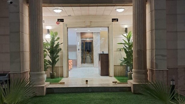 Une entrée d’immeuble avec un chemin central bordé de colonnes, menant à une porte en verre.