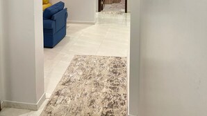 Un couloir avec un canapé bleu, un tapis à motifs et une porte donnant sur un espace cuisine.