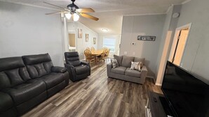 Ein Wohnzimmer mit Sofa, zwei Sesseln, Fernseher und Deckenventilator.