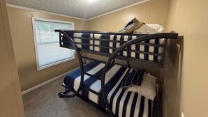 Ein Stockbett mit gestreifter Bettwäsche in einem Zimmer mit beigen Wänden und einem Fenster mit Jalousien.