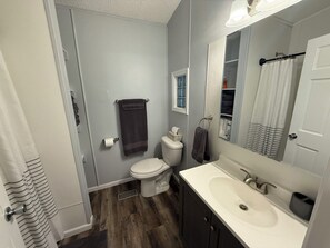 A bathroom with a toilet, sink, and mirror. There is a towel rack with towels, a shower curtain, and a window above the toilet.