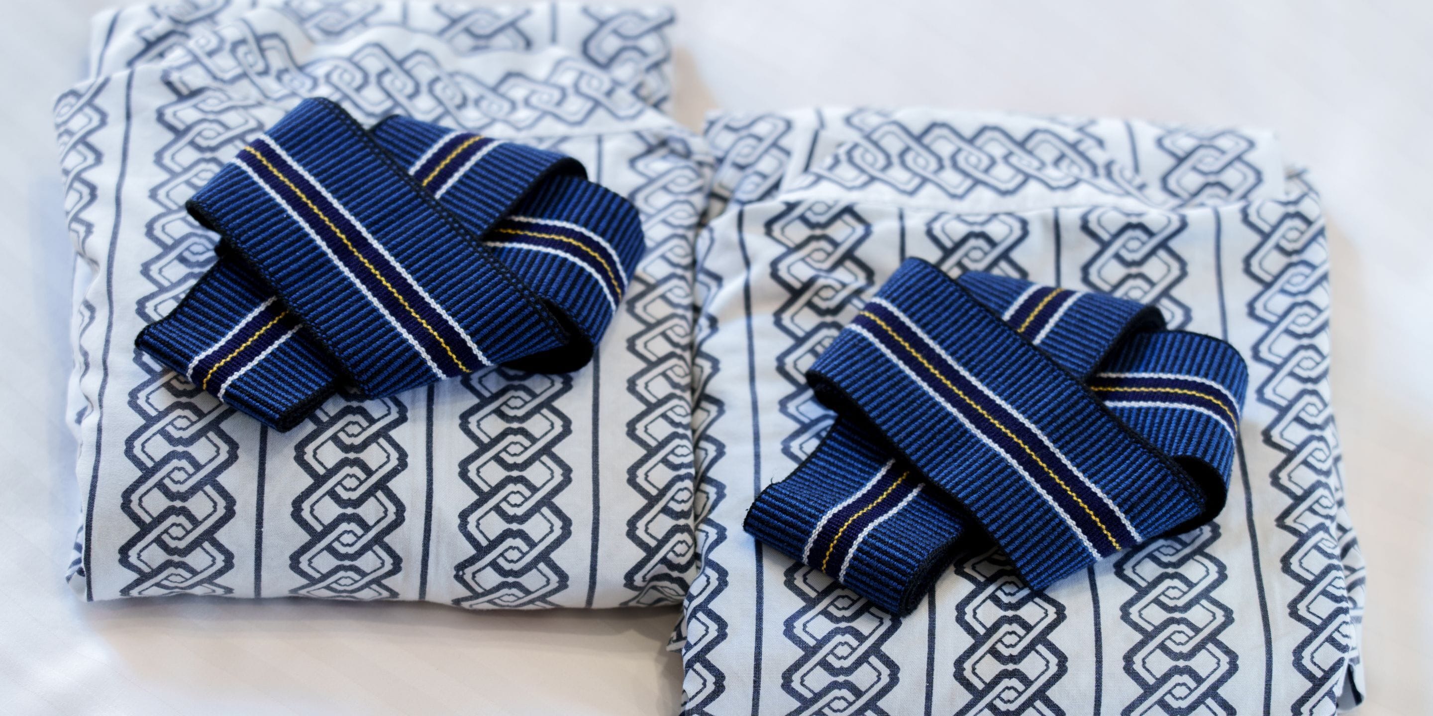 Two neatly folded shirts with a geometric pattern and a blue and yellow striped bow.
