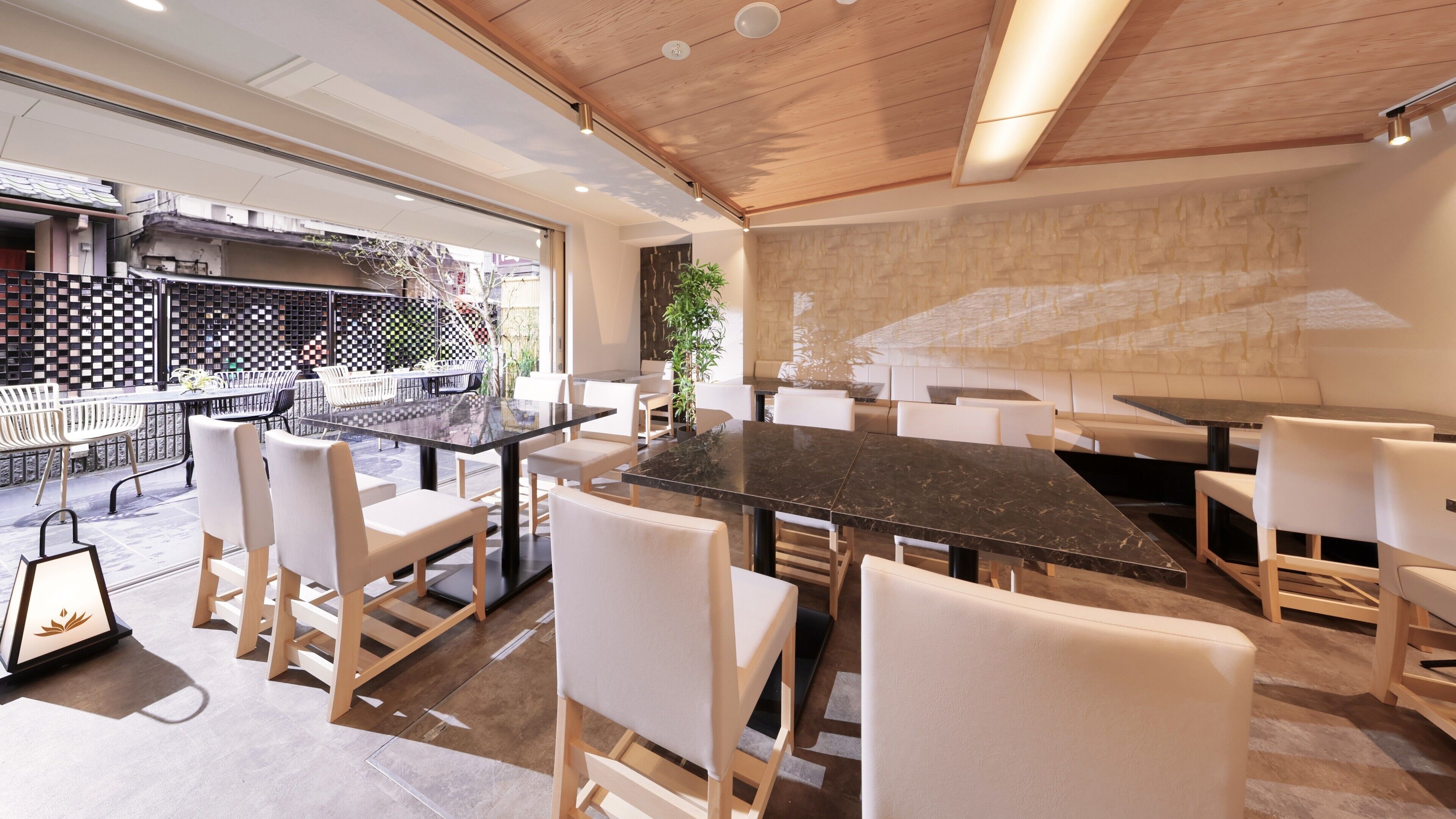 Un espace repas moderne avec une grande table en marbre et des chaises blanches, un plafond en bois et une vue sur l’espace extérieur aménagé pour les repas.