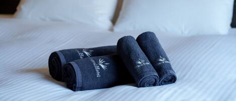 A neatly made bed with white linens and two rolled towels with embroidered text.