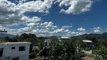 Un quartier résidentiel avec des maisons blanches, une végétation luxuriante et un ciel bleu clair parsemé de quelques nuages.
