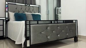Une chambre à coucher moderne avec un lit recouvert d’un tissu gris, du linge de lit blanc et un grand miroir.