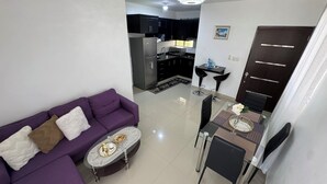Un salon moderne avec un canapé violet, une table basse en verre et un coin repas comprenant une table et des chaises en verre.