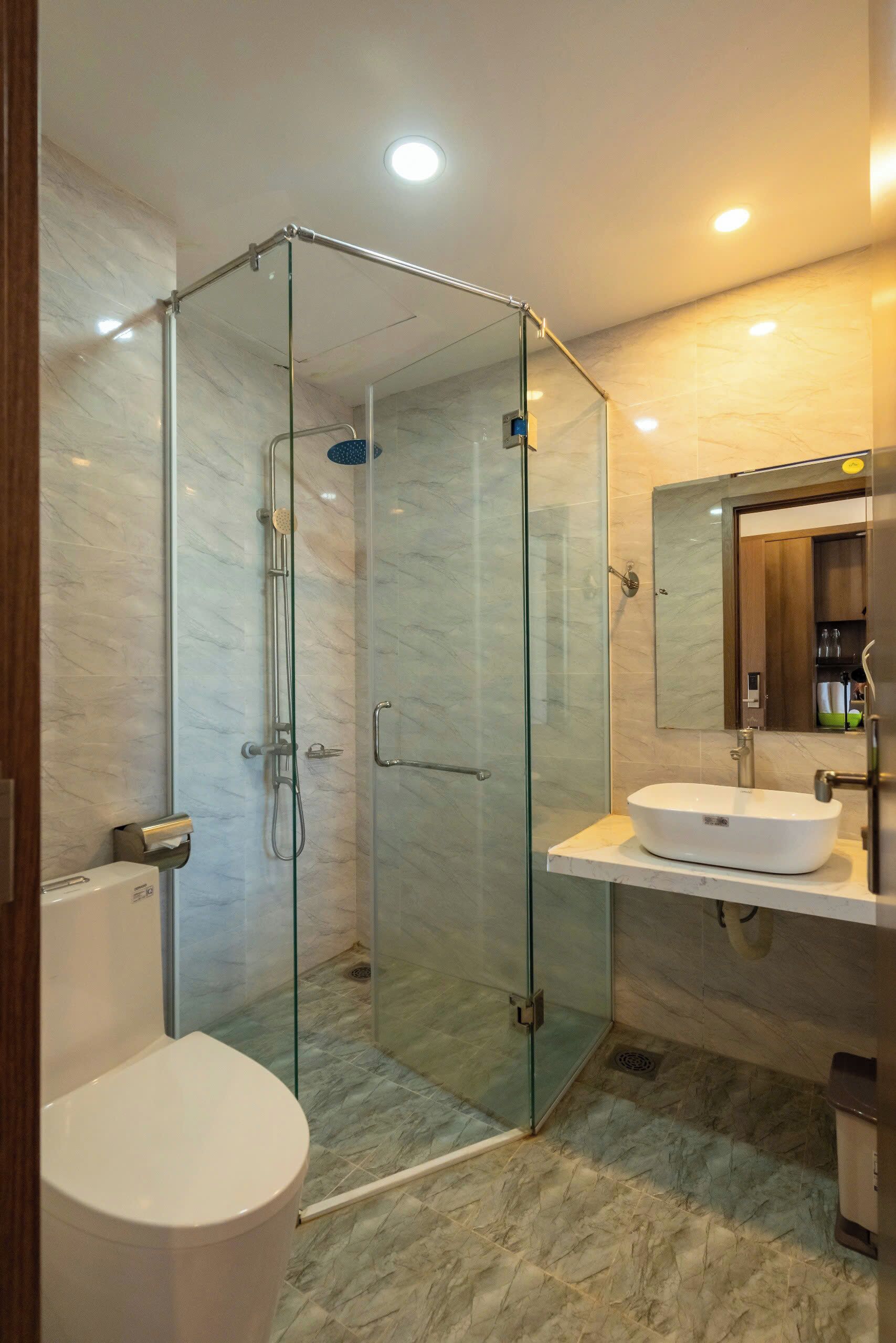 A modern bathroom with a glass-enclosed shower, a white sink, and a marble-tiled floor.